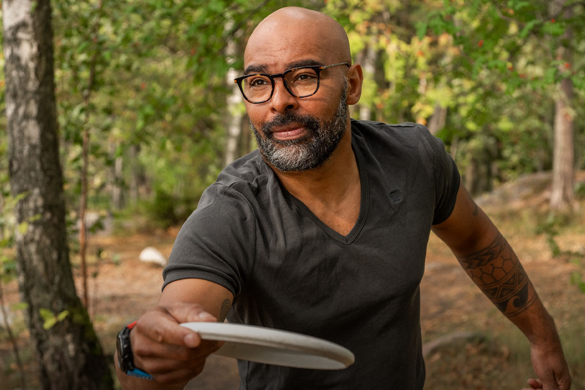 Silmälasipäinen mies frisbeegolf radalla metsässä